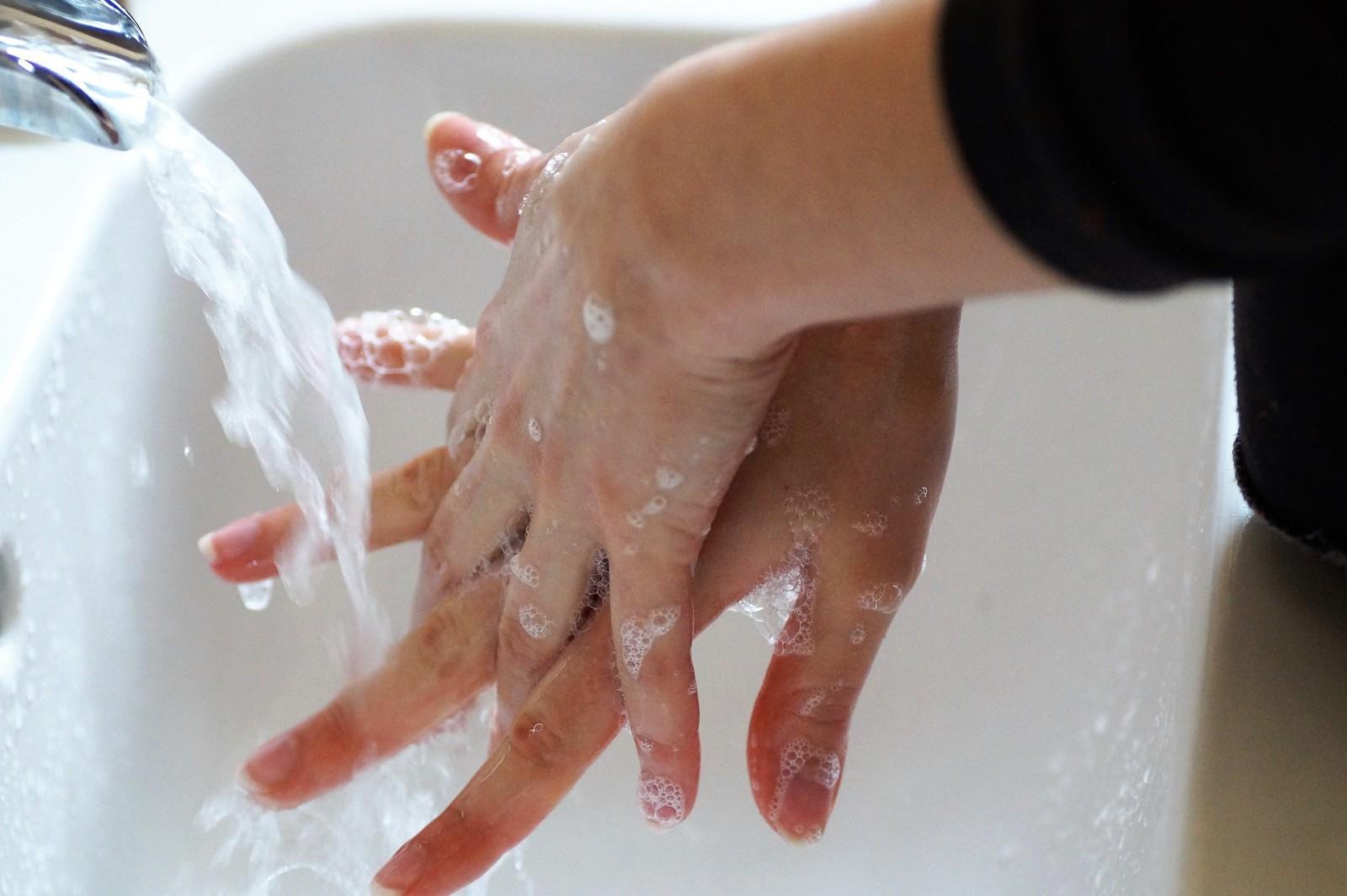 Henkilö vaahdottaa saippuaa käsiinsä lavuaarissa auki olevan hanan alla.