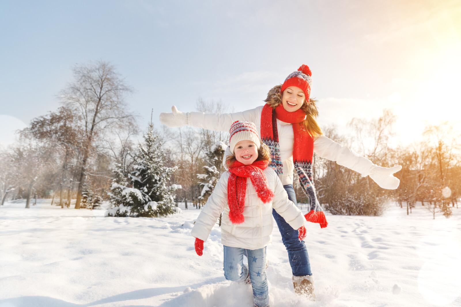 Nainen ja pieni lapsi juoksevat lumessa nauraen.