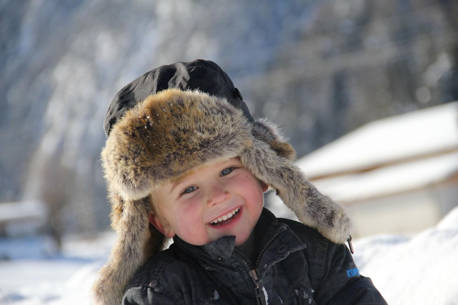 Karvalakki päässä oleva poika nauraa. Taustalla talvista maisemaa.
