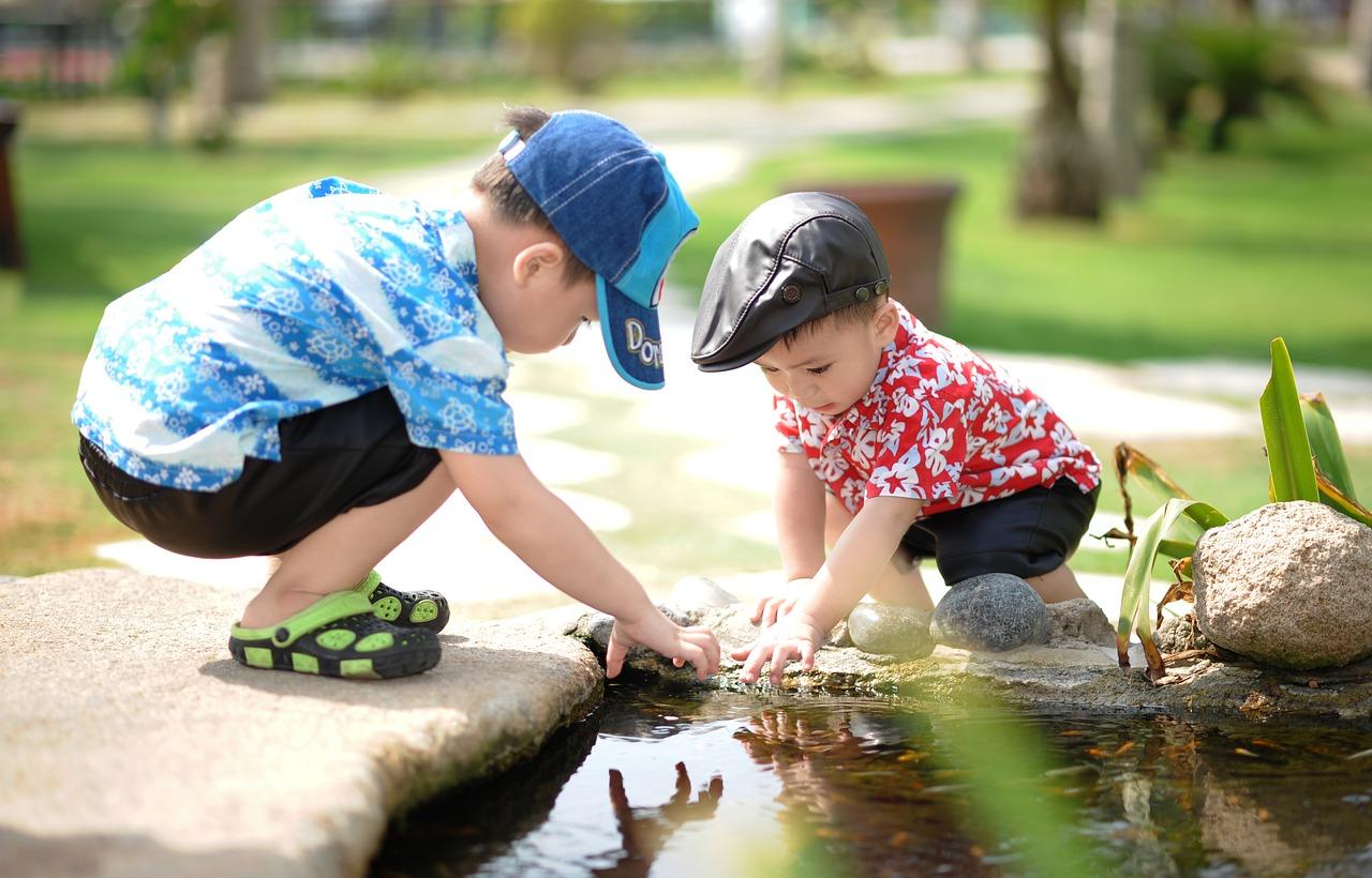 Kaksi pientä poikaa leikkii pienen puron äärellä.